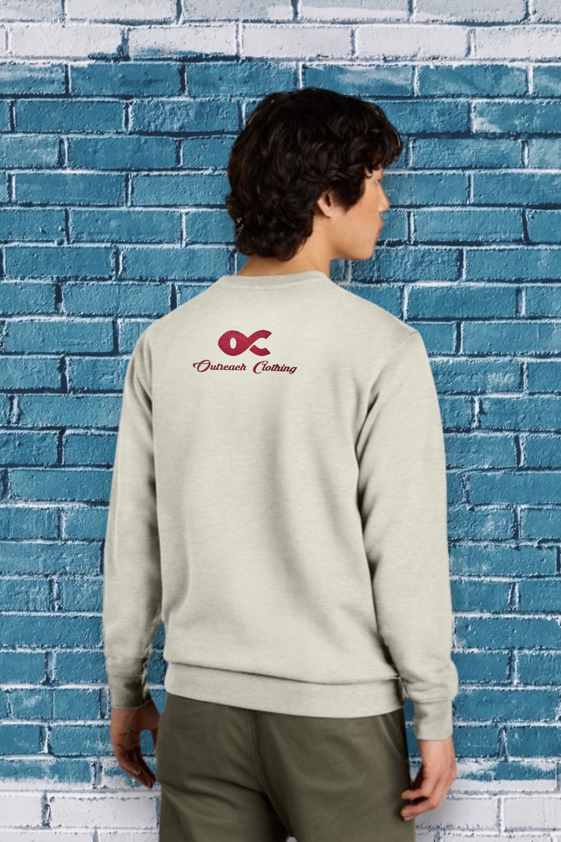 Person wearing a light gray sweatshirt with a logo against a blue brick wall