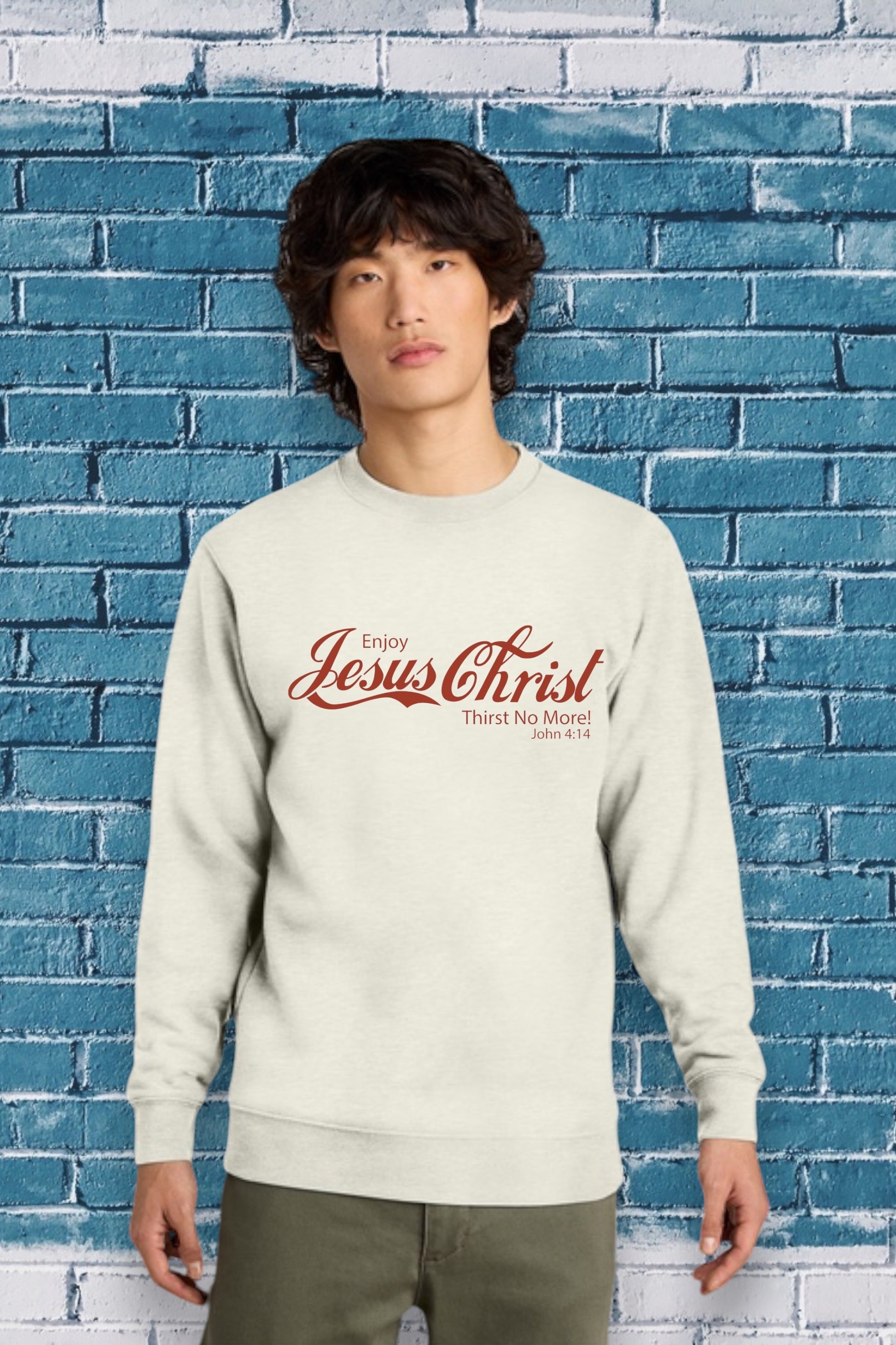 Person wearing a beige sweatshirt with text in front of a blue brick wall