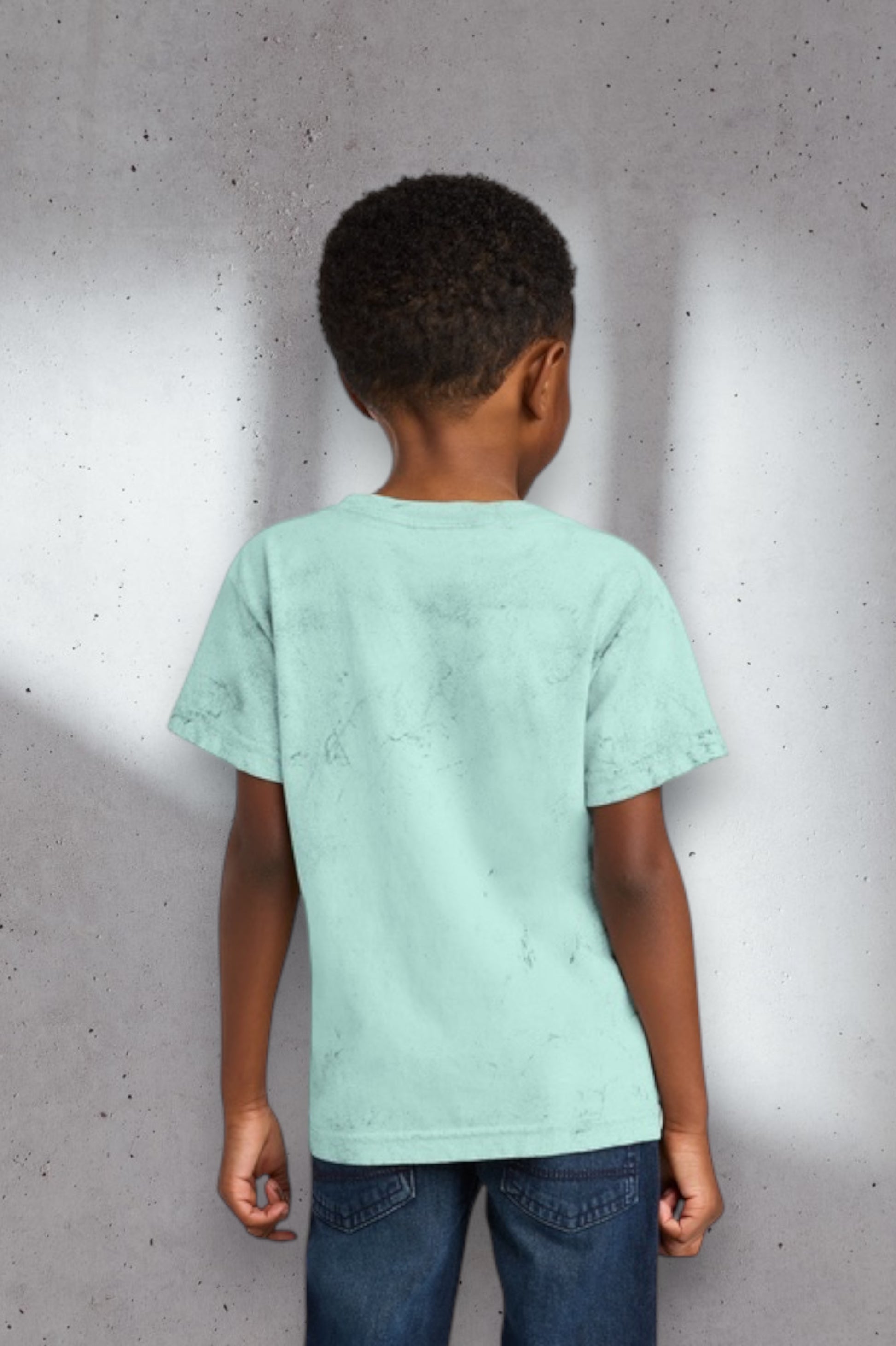 Child wearing a light green t-shirt against a gray wall